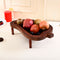 Wooden fruit tray with pomegranates and other fruits on a white surface.